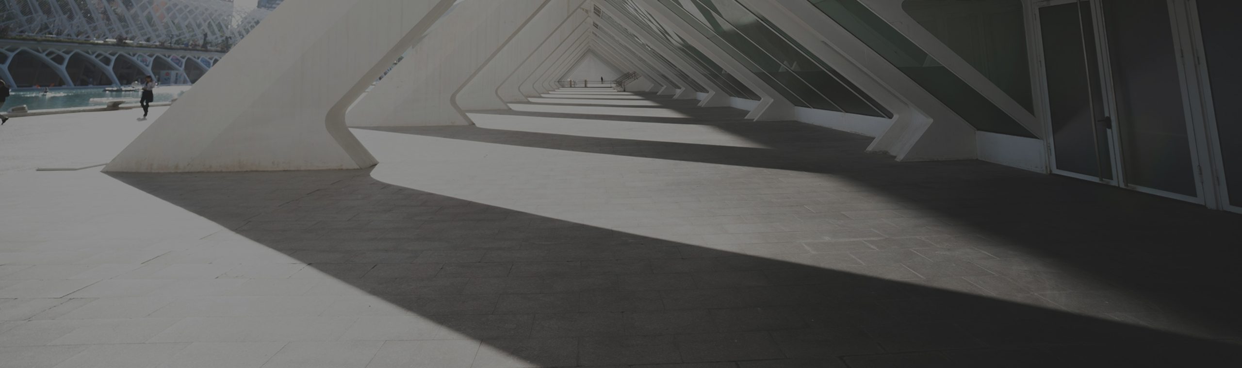 A futuristic white architectural walkway with strong geometric shadows stretching across the ground.