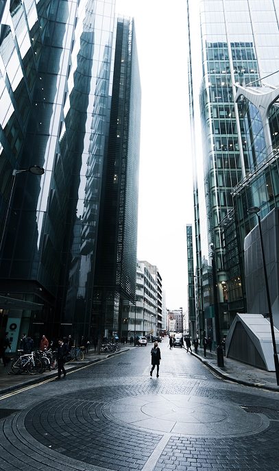 A low-angle shot of a city street lined with modern glass skyscrapers, with a person walking in the middle.