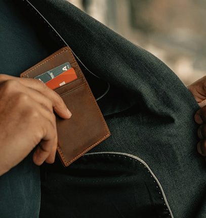 Hand placing or removing a brown leather wallet with credit cards from a dark jacket pocket.