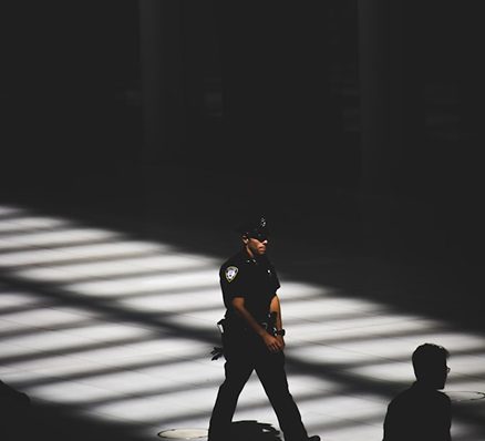 A police officer walks through a dimly lit space with geometric light patterns on the floor.