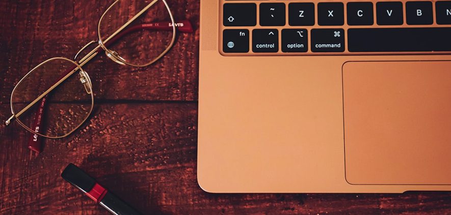 Eyeglasses, laptop keyboard, and marker on a wooden desk, signifying work or study.