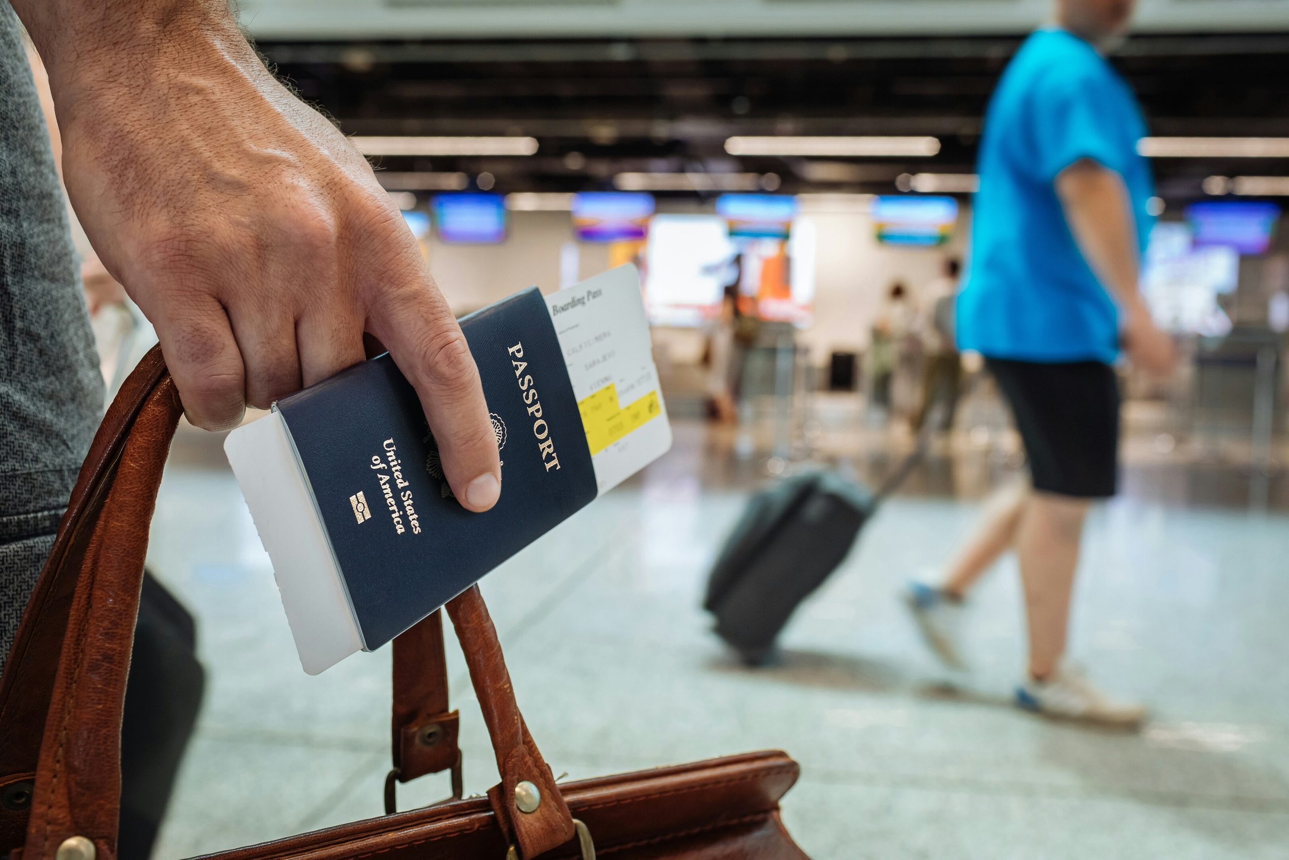 A hand holds a U.S. passport and boarding pass, ready for travel in a bustling airport.