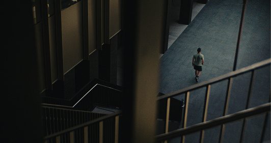 A man walks away on a concrete floor in a modern, multi-level building with stairs and railings.