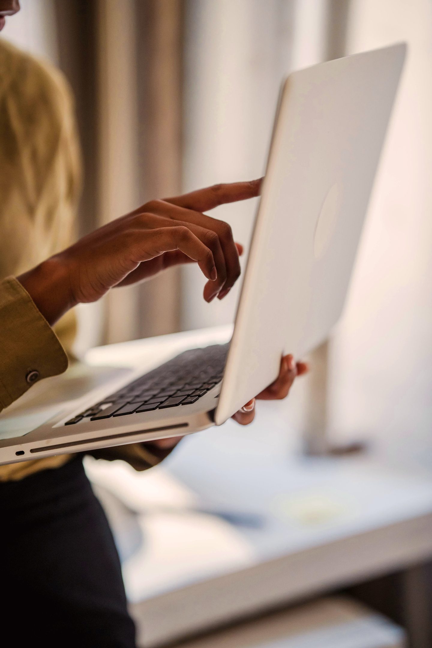 Dark-skinned hands on open laptop screen.