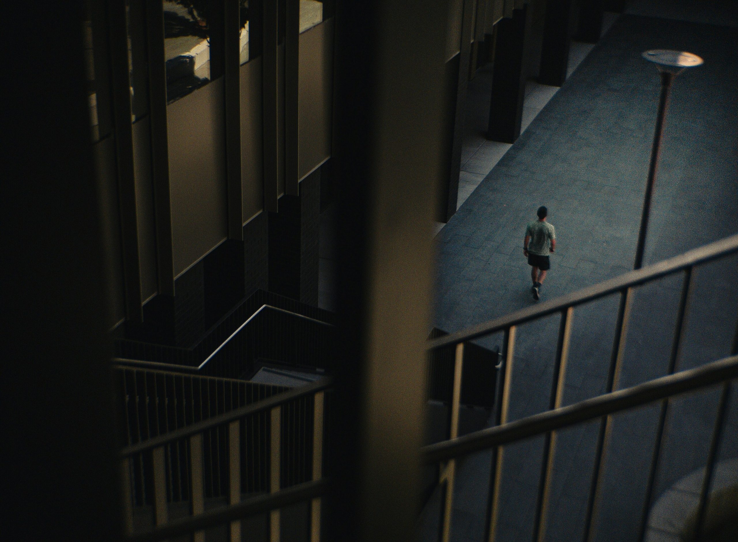 Overhead view of a person walking away on a dark urban walkway, framed by architectural stairs and railings.