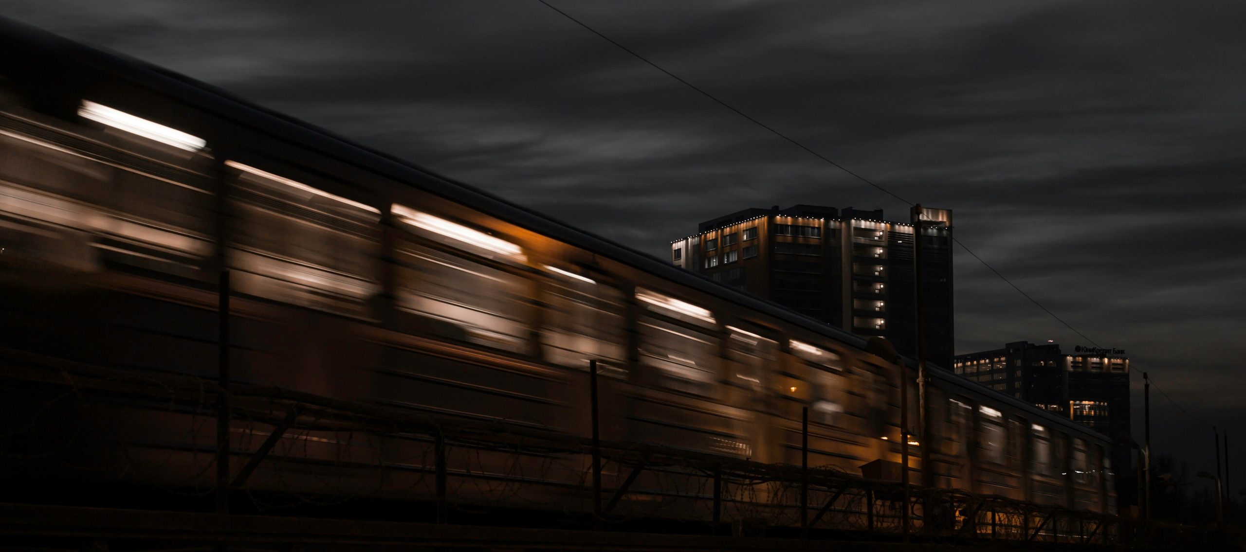 Long exposure of a fast-moving train with light trails against a dark sky and illuminated buildings.