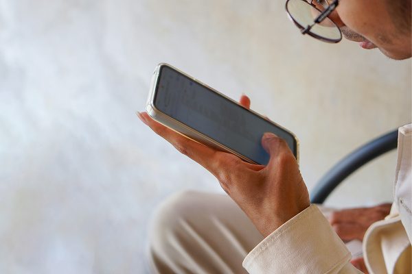 A person wearing glasses holds a smartphone horizontally, viewing its screen and interacting with it.