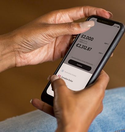 Hands hold a smartphone showing a currency exchange app with pounds and euros, selecting Canadian Dollar.