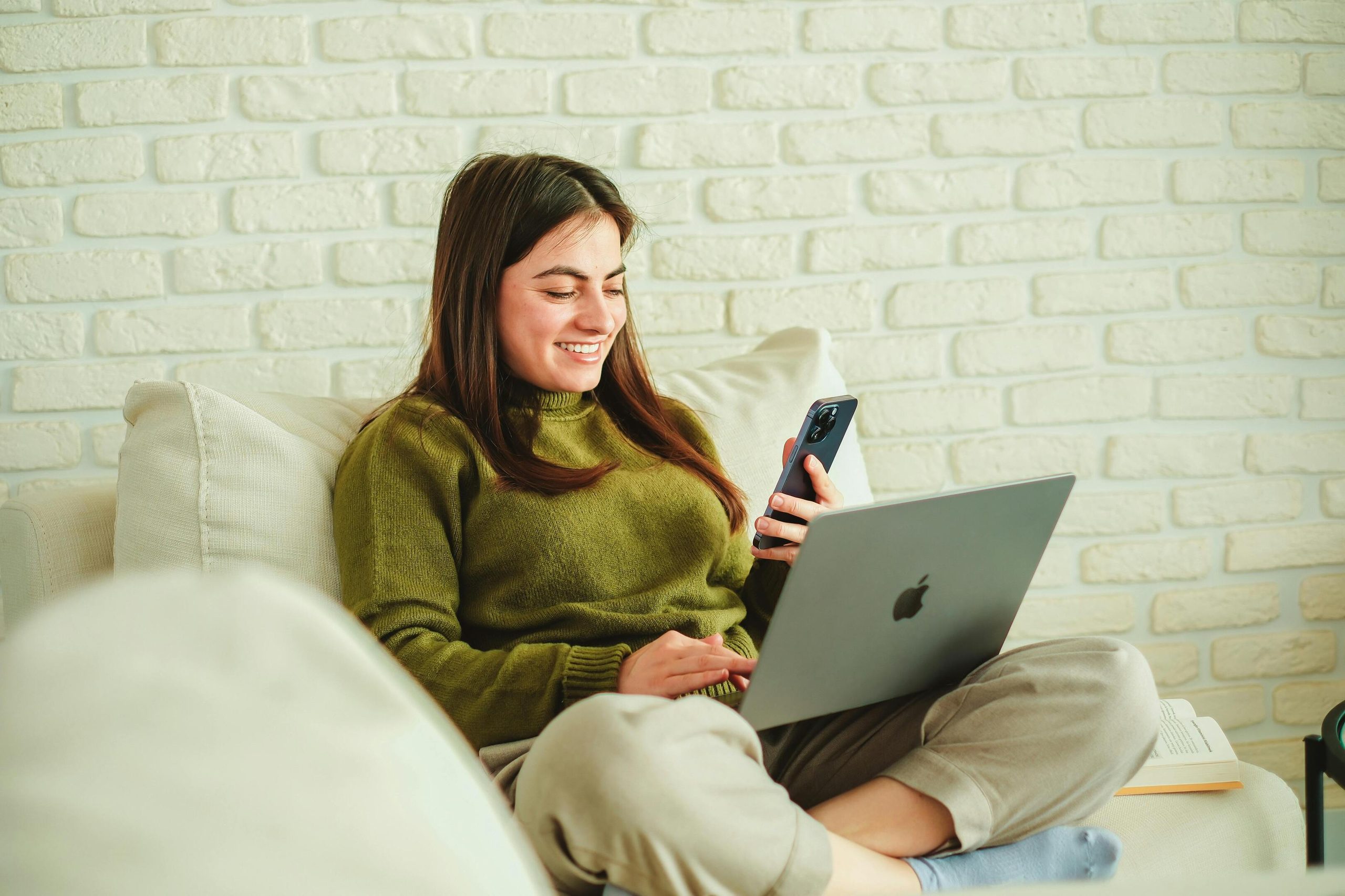 Smiling woman on sofa with phone and laptop.