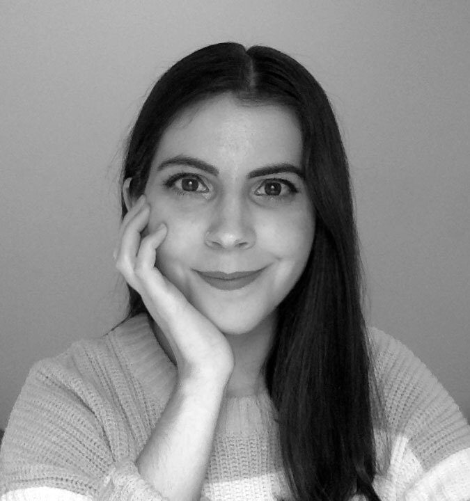 Smiling woman in B&W with dark hair and hand on chin.
